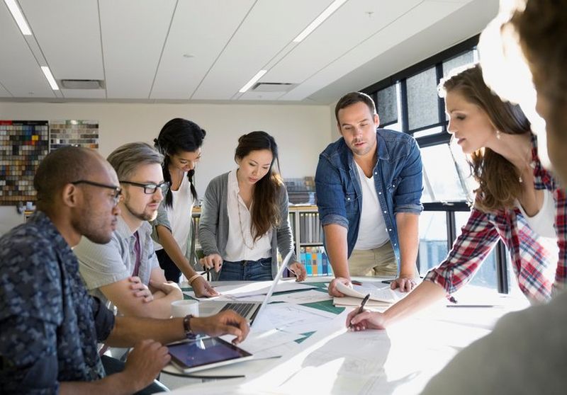 Casually dressed office workers huddle round a table to look through documents.