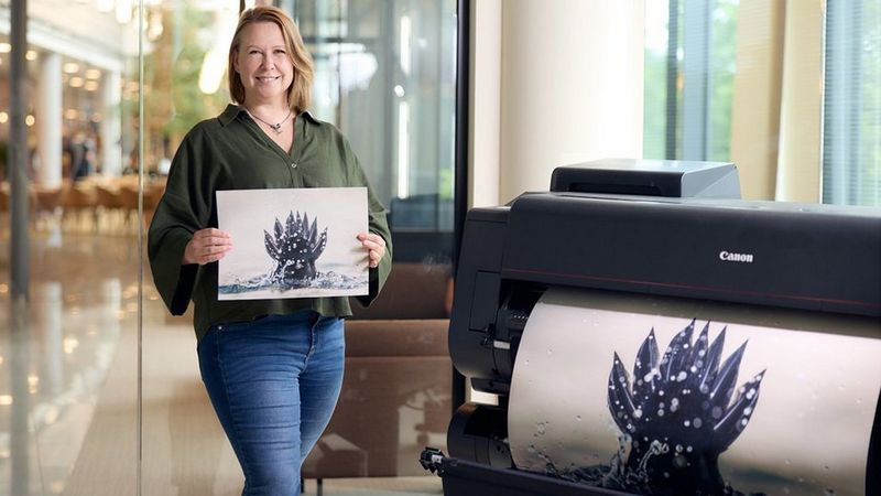 Palkittu luontovalokuvaaja Mia Surakka esittelee tulostettua kuvaansa sukeltavasta linnusta. Kuvan etualalla Canon suurkuvatulostin.
