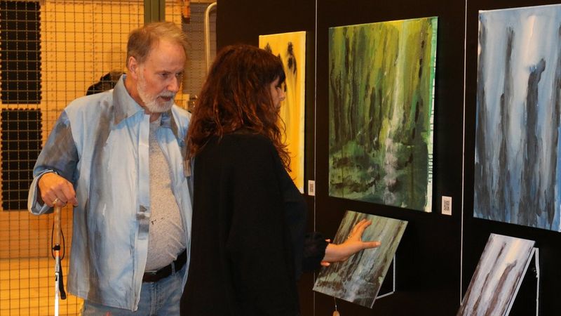 Micce Rylander e un ospite esplorano con le mani le opere astratte tattili. Sopra le versioni stampate a rilievo sono esposti i dipinti originali.