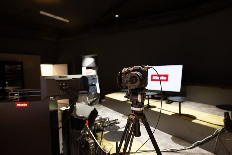 Камера Canon Cinema EOS с объективом RF установлена на штатив и подключена проводом к внешнему монитору. На ЖК-экране на фоне можно увидеть логотип Miele.