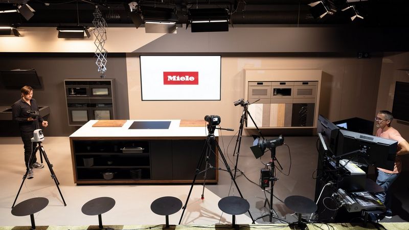 Несколько камер Canon, включая Cinema EOS C70, CR-N300 и EOS R5C, стоят на штативах на кухне-студии, подготовленной Miele AG, а между ними работают двое участников съемочной группы.