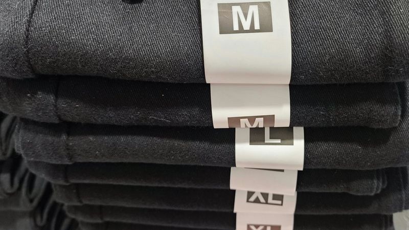 Una pila di jeans neri piegati con etichette bianche con le taglie M, L e XL.