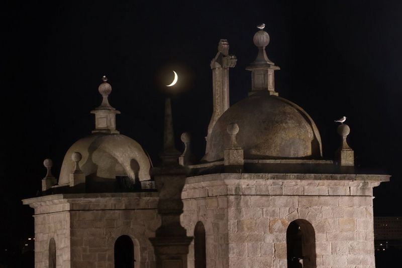 A sliver of a crescent moon visible between two pillars of a church, taken on a Canon EOS R10.