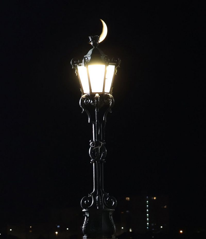 A sliver of a crescent moon peaking out from behind a lamp post, taken with a Canon RF 24-105mm F4-7.1 IS STM lens.