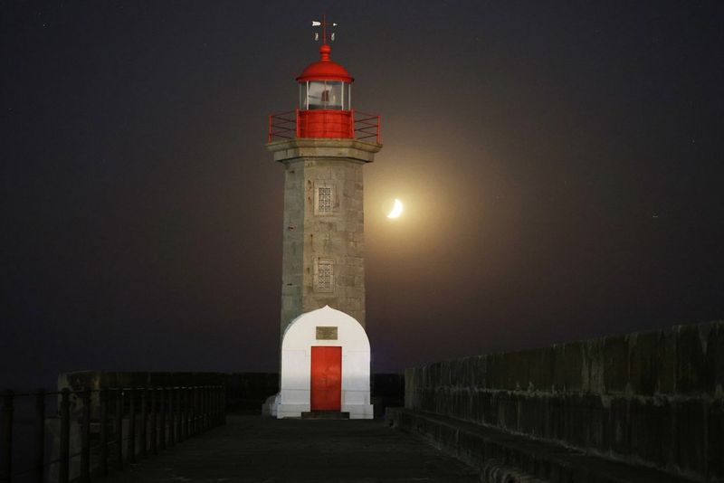 The crescent moon visible in the night sky behind a lighthouse, taken on a Canon EOS R8.