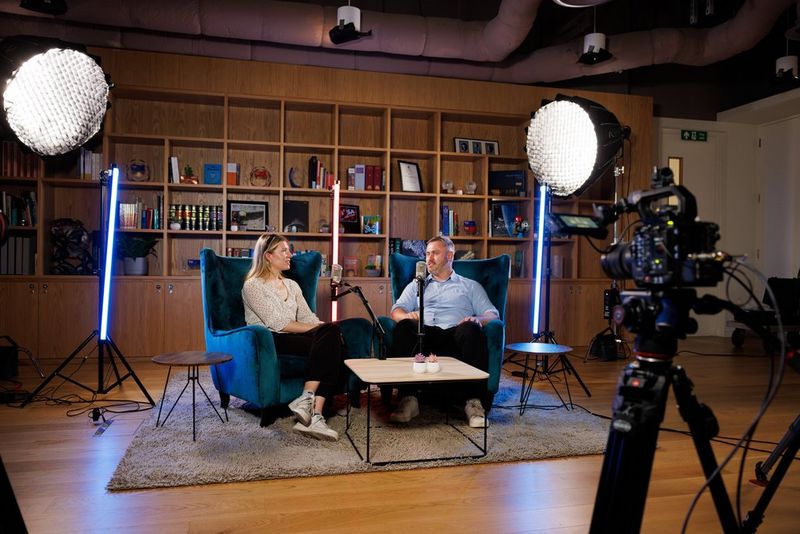 Twee mensen zitten in leunstoelen in een interviewopstelling voor een videopodcast met Canon-camera's en -objectieven.