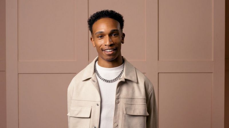 Fashion photographer Ian Hippolyte stands in front of a panelled wall.