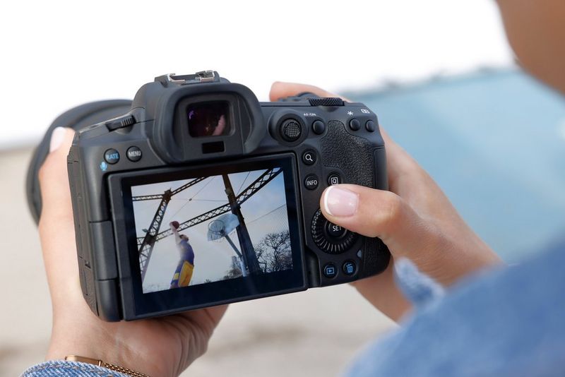 Hands hold the back of a Canon EOS R5 camera, looking at an image on the viewscreen of a man jumping up at a hoop with a ball in both hands.