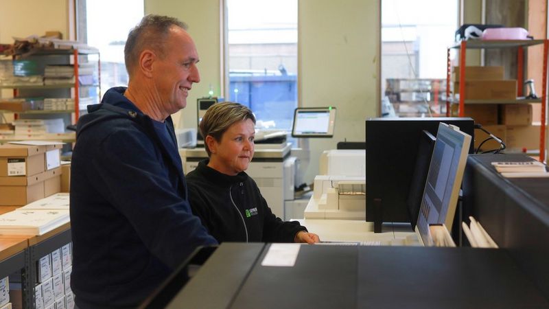 To mennesker som står og ser på en dataskjerm 