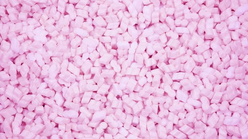 A close-up of densely packed pink packing peanuts, shaped like small puffy beads.