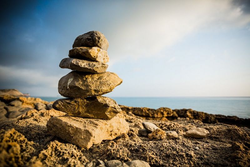 Op elkaar gestapelde stenen vlakbij de zee. Er is sprake van een donkere vignettering in de hoeken van de afbeelding en van lichte cilindervertekening.