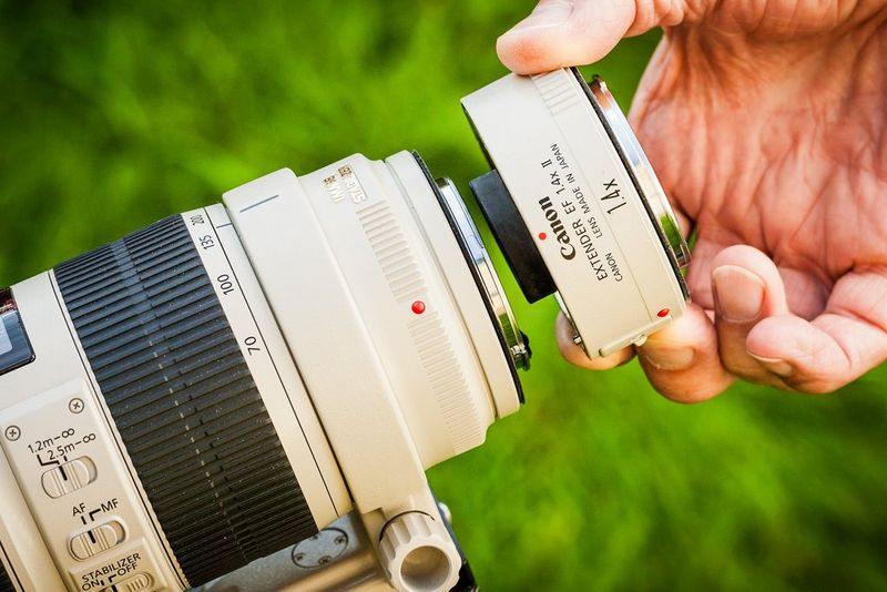 Close-up of a photographer's hand attaching a Canon Extender 1.4x II to a telephoto lens.