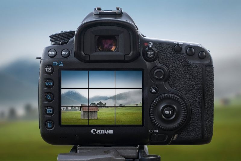 במסך ה-LCD האחורי של מצלמת Canon מוצגים קווי רשת מעל תמונה של בקתה בנוף הררי.