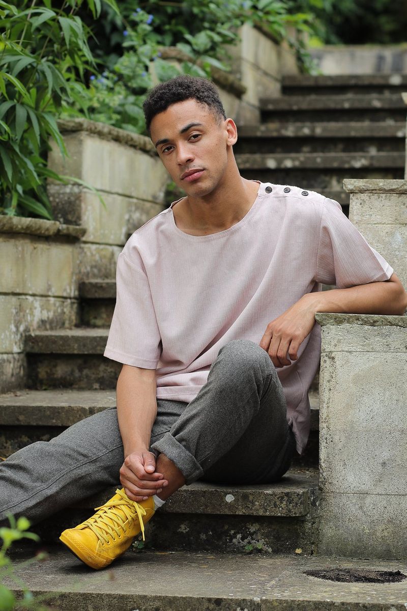 A casually-dressed young man sitting at the foot of a flight of concrete steps outdoors in daylight, with the deepest shadow areas lightened, revealing more detail.