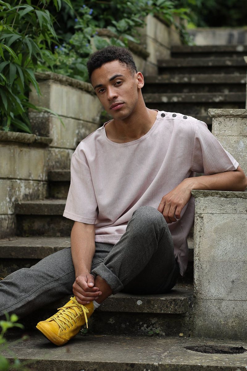 A casually-dressed young man sitting at the foot of a flight of concrete steps outdoors in daylight, which has caused deep shadows.