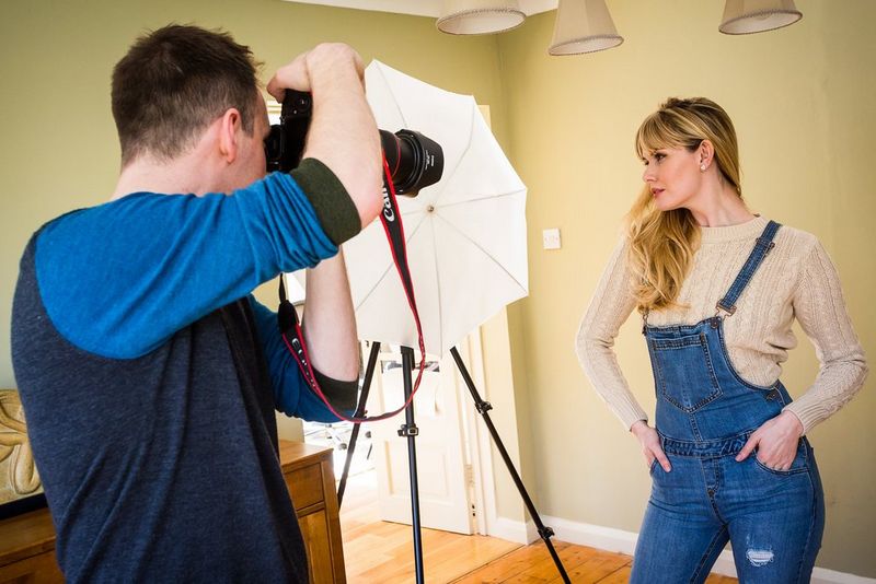 A photographer taking a portrait of a woman using low-key setup, with Canon camera, lens, and flash. © Marcus Hawkins