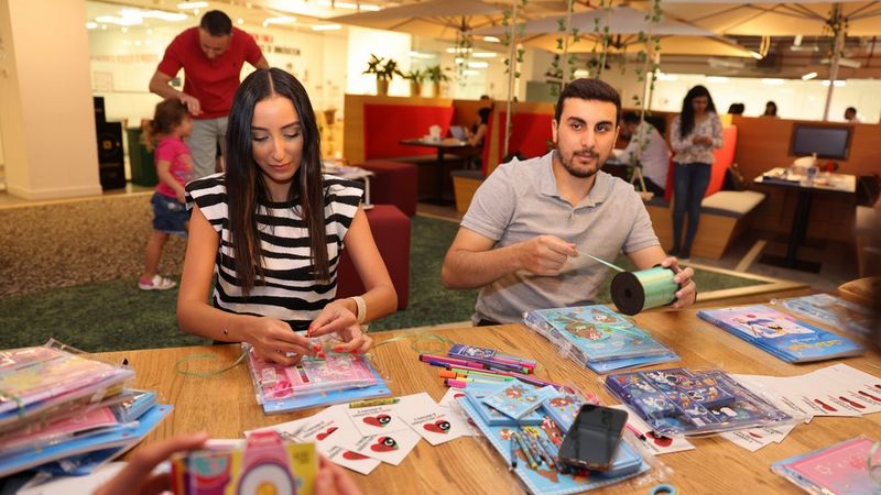 A man and a woman sit at a table, surrounded by craft items.