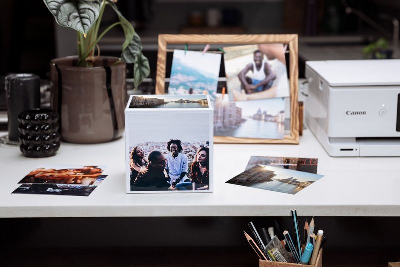 A Canon Photo Cube on a desk and a Canon printer, plants, photo frames and other office trinkets next to it.