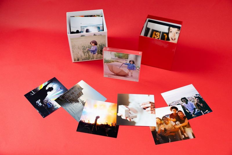 Two Canon Photo Cubes sit on a red surface, surrounded by other photo prints. 