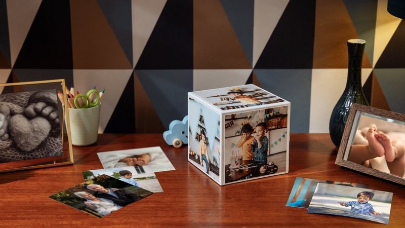 A Canon Photo Cube sitting on a sideboard next to photo frames, a vase and other photo prints. 