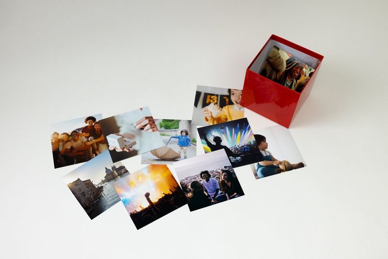 Photographs scattered on the table in a pile with a Canon Photo Cube containing more photographs.