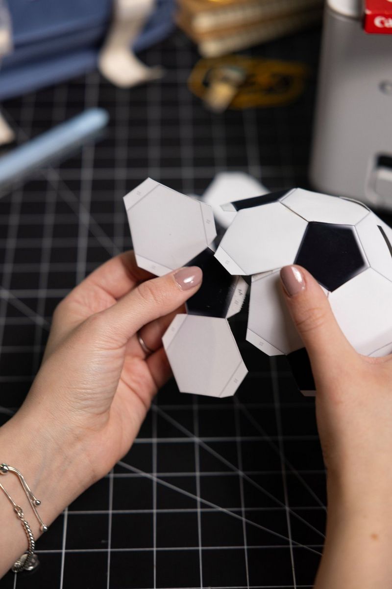 Handen die een papieren voetbal van een geprinte Canon Creative Park-sjabloon monteren op een snijmat.