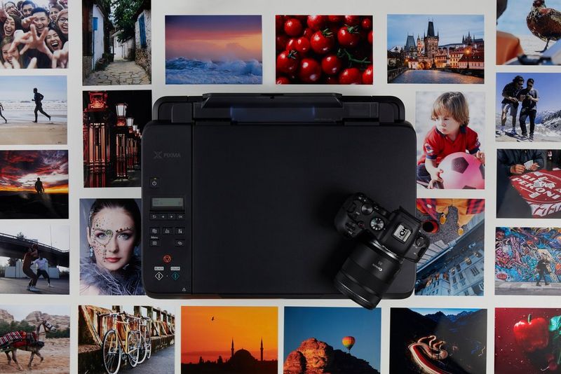 A top-down view of a Canon printer and camera surrounded by a montage of colourful landscape, travel and portrait prints.
