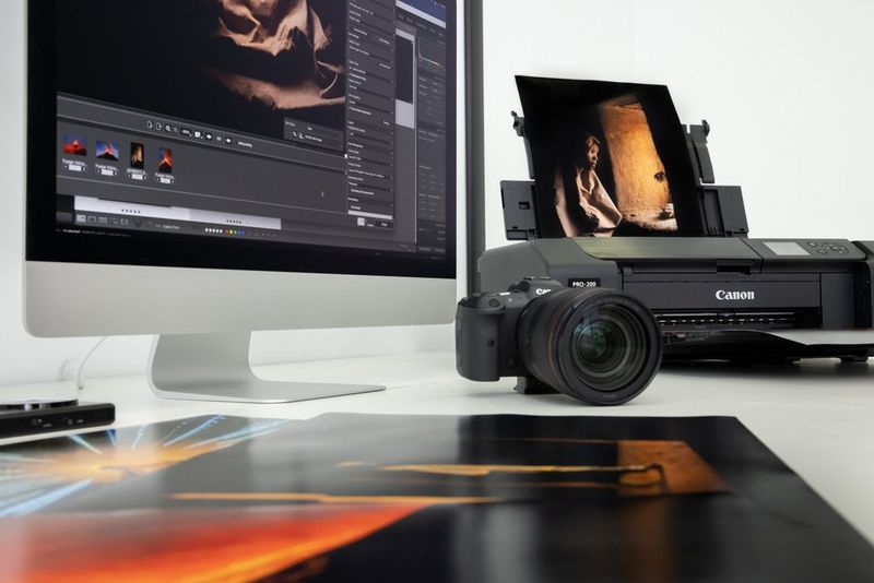 Geprinte foto's op een bureau naast een computer, Canon PIXMA PRO-200-printer en een Canon-camera.