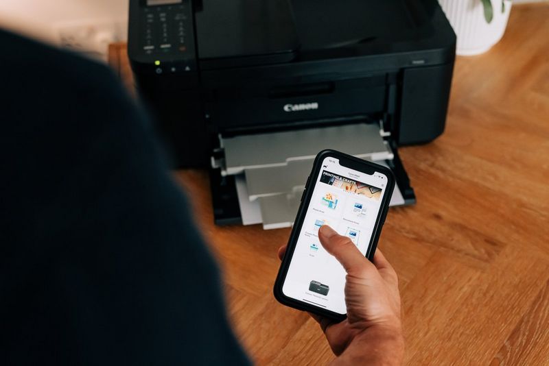 A person using a smartphone to print to a Canon home printer.