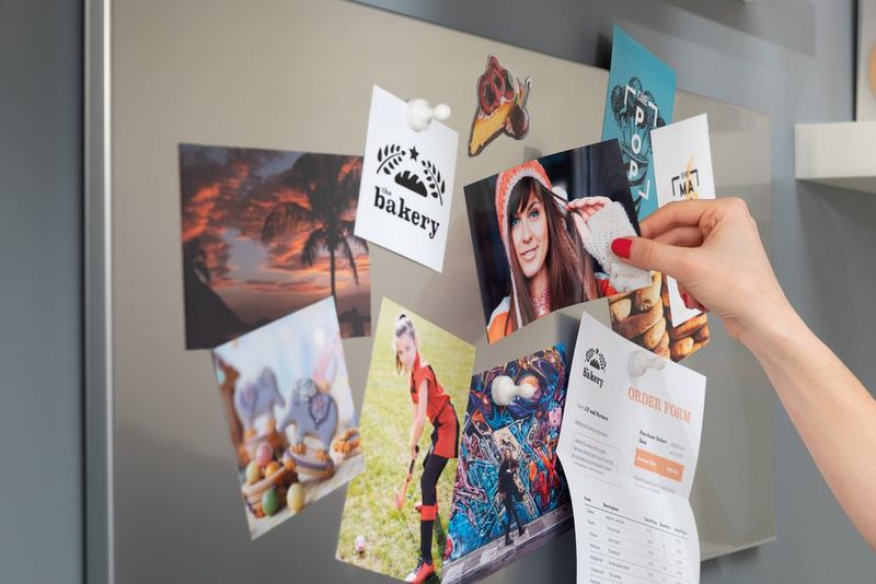 A hand puts up a printed photo on a pinboard which has other prints pinned up. 