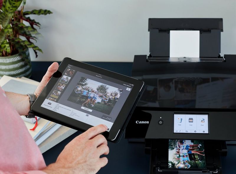 אדם מחזיק טאבלט עם צילום של קבוצת חברים במסך. ברקע מדפסת Canon PIXMA המדפיסה תמונה זו כעת.