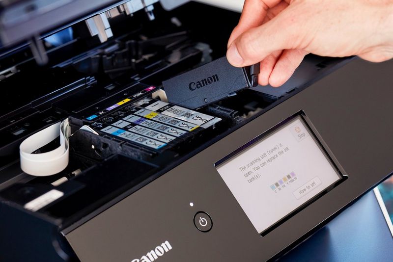 A hand replaces one of six ink cartridges in a Canon inkjet photo printer.