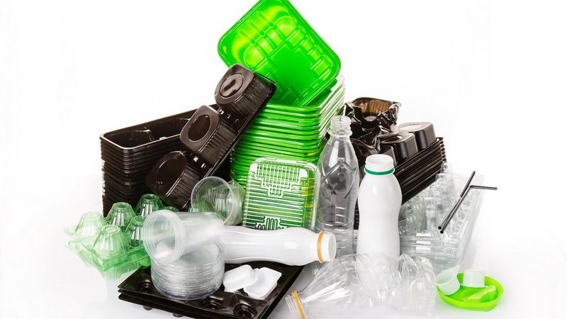 A huge pile of clear, lime green, white and black plastic bottles, containers, lids and straws. These are neatly stacked and photographed against a white background.