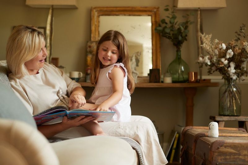 Искренняя близость матери и дочери, сидящих на стуле и читающих книгу; на журнальном столике стоит камера Canon PowerShot PX.