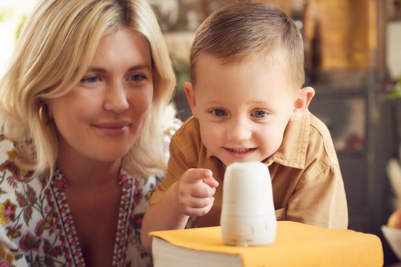 A woman and young boy look excitedly at the Canon PowerShot PX, positioned on a pile of books.