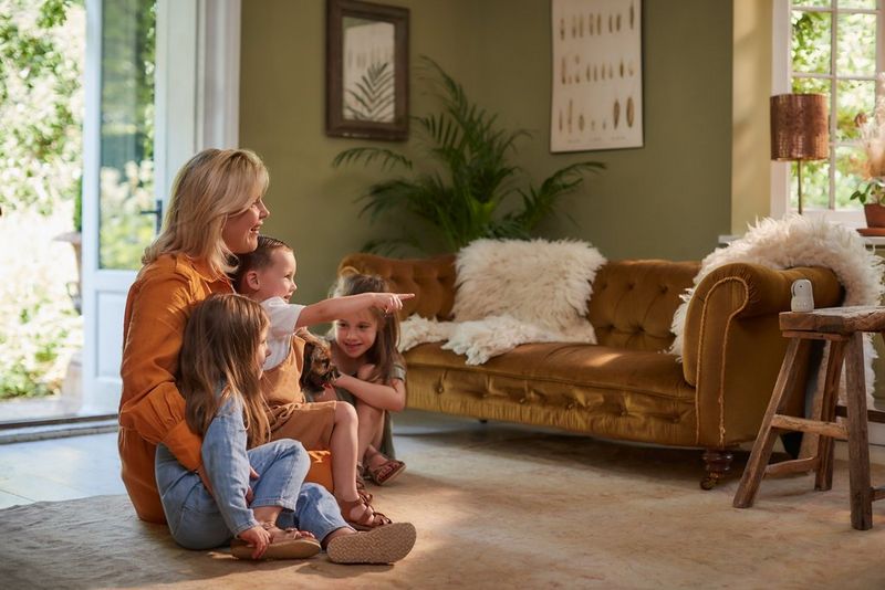 A mother sits with her three children in a lounge, posing for a portrait on the Canon PowerShot PX. There is a sofa in the background.
