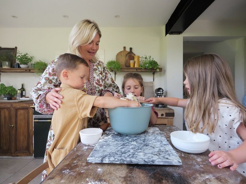 A family sit and stand around a breakfast bar, mixing baking ingredients in a bowl. 