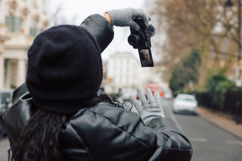 A person holds a Canon PowerShot V1 vertically in one hand, filming herself.