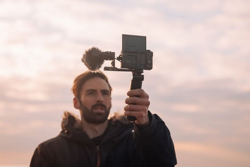 Muž v dlouhém kabátě, který s fotoaparátem Canon PowerShot G7 X Mark III natáčí na ručním gimbalu.