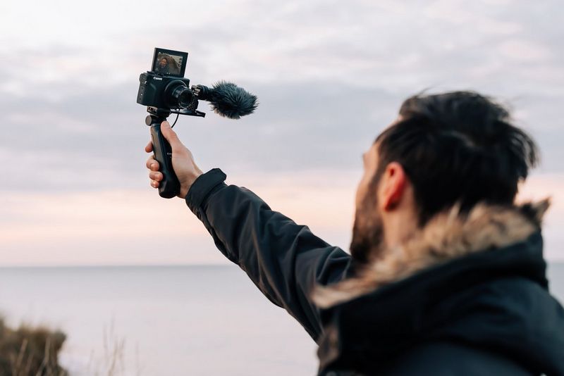 Мужчина идет по пляжу и снимает себя на камеру PowerShot G7 X Mark III.