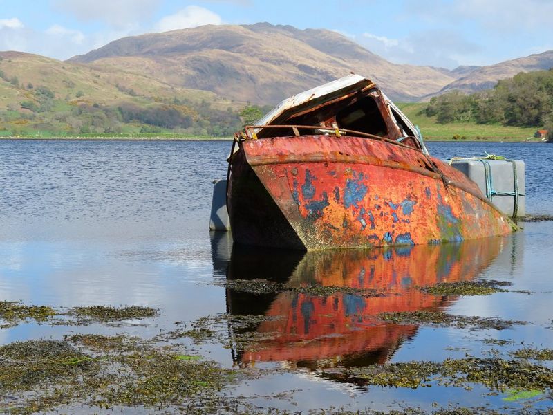 סירה חלודה בגוון אדום עוגנת באמצע אדם ביום שמשי. צולם באמצעות Canon PowerShot SX740 HS LITE EDITION.