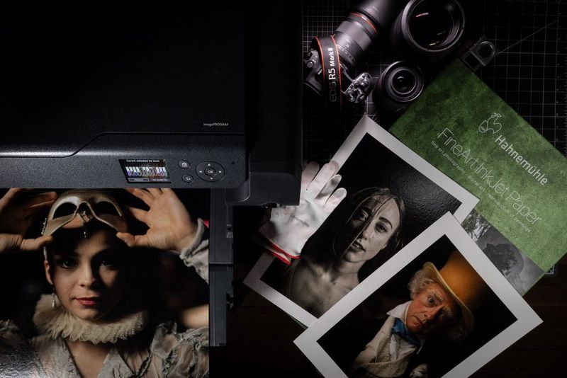 На лотке принтера Canon imagePROGRAF PRO-1100 лежит отпечатанный портрет; рядом — несколько других работ. В кадре также — камера Canon EOS R5 Mark II, объективы серии RF и бумага для струйной печати Hahnemuhle FineArt.