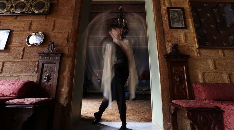 Blurred figure moving through a decorated room with vintage furniture and framed art.