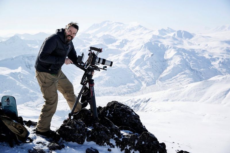 Alex Wykes with his fully rigged-up Canon EOS-1D X Mark III on top of a snowy mountain in Russia.