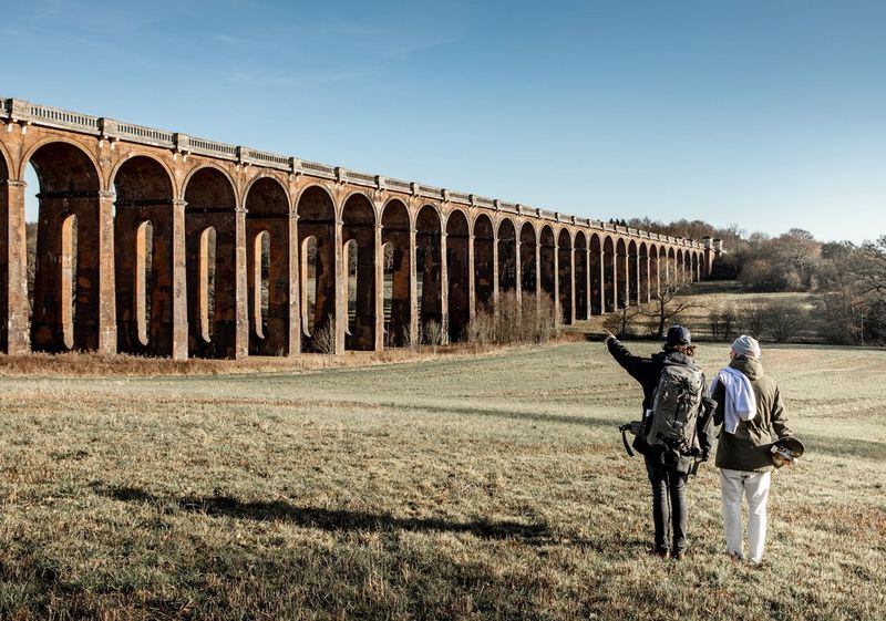 Two people stand in a valley looking at the Balcombe Viaduct in West Sussex, England.