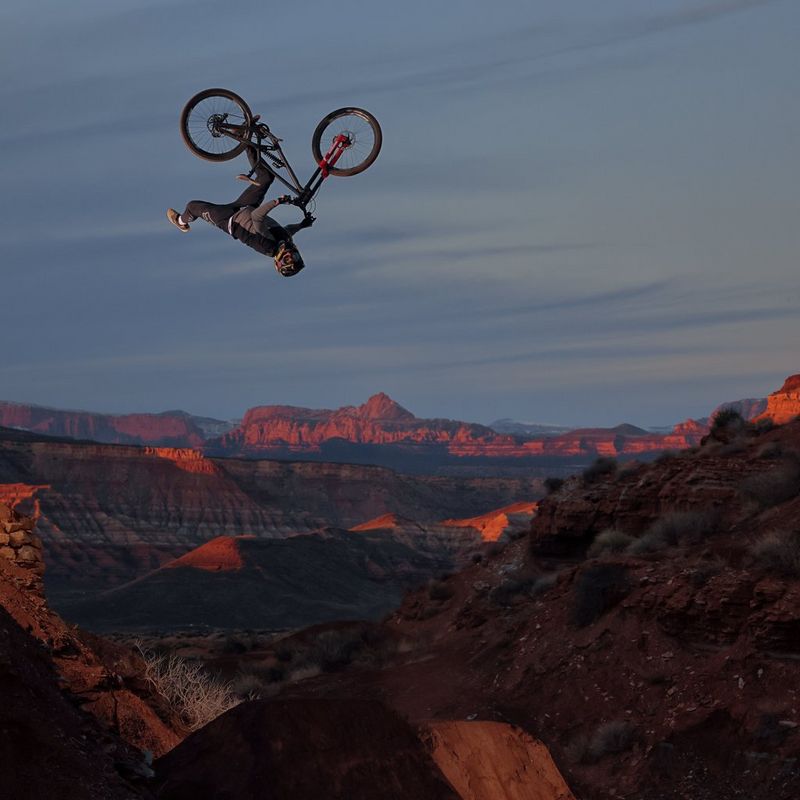 An upside down mountain bike and rider travelling through the air above a rocky desert landscape.