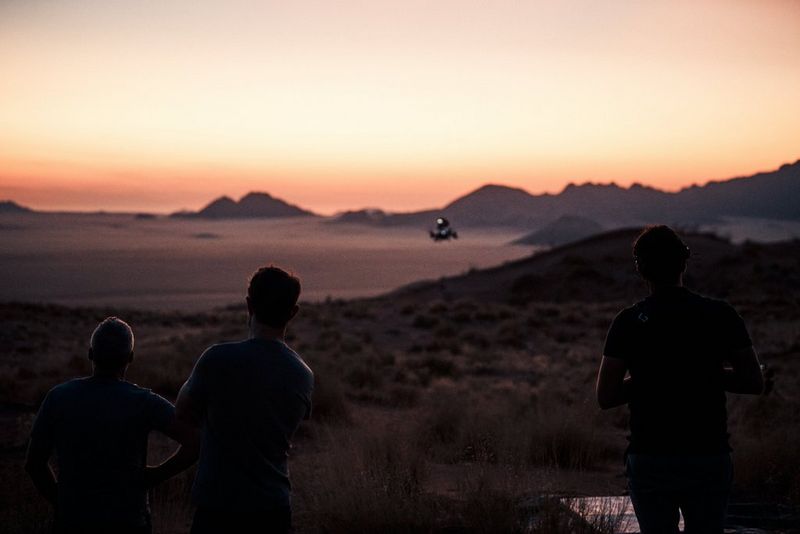 Landschap met drie mensen die afsteken tegen de zonsondergang met in de verte een vliegende drone.