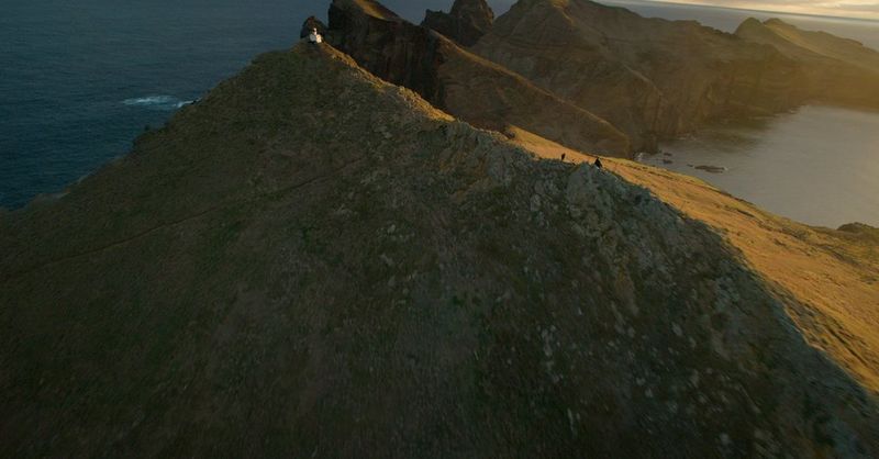 A still from drone footage, shot by drone pilot David Gu, of a lighthouse at the end of a long mountain ridge.