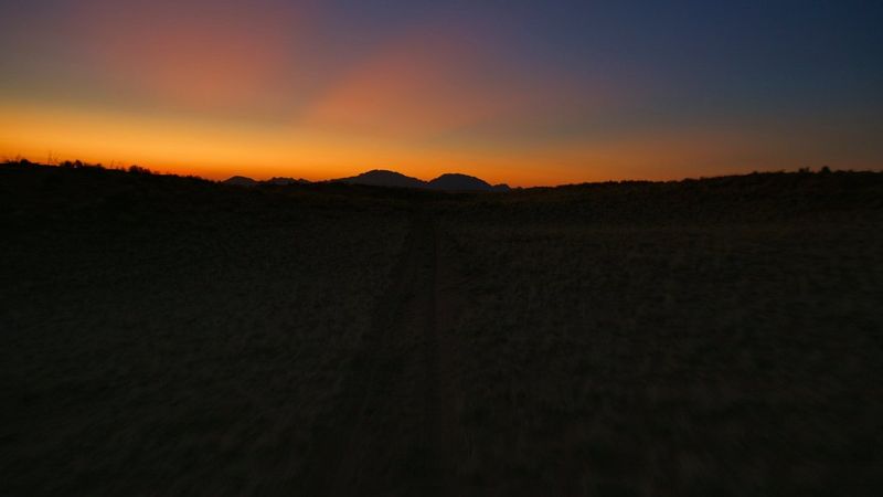 A still from drone footage, shot by filmmaker Brett Danton, of hills and trees silhouetted against an orange and dark blue sky.