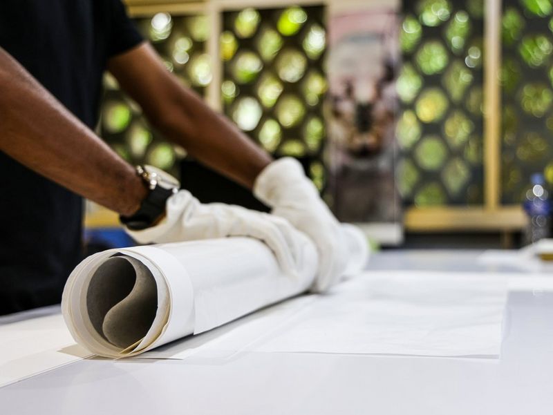 Due mani con guanti bianchi arrotolano una grande stampa fotografica.